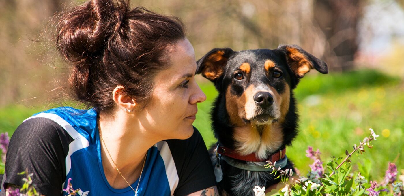 Frau und Hund liegen nebeneinander auf dem Bauch auf einer Wiese